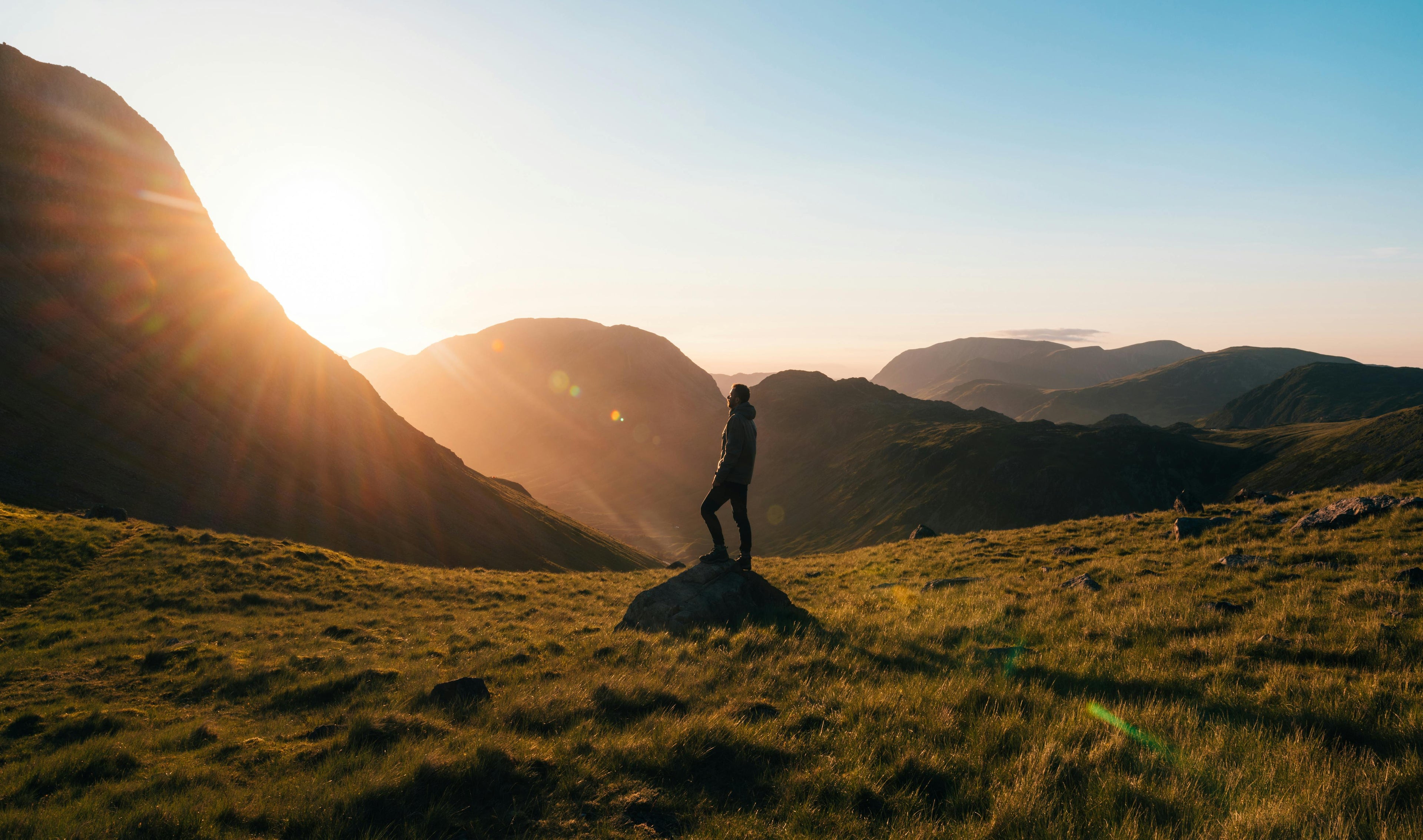 Person standing on a mountain top with the sun setting behind them