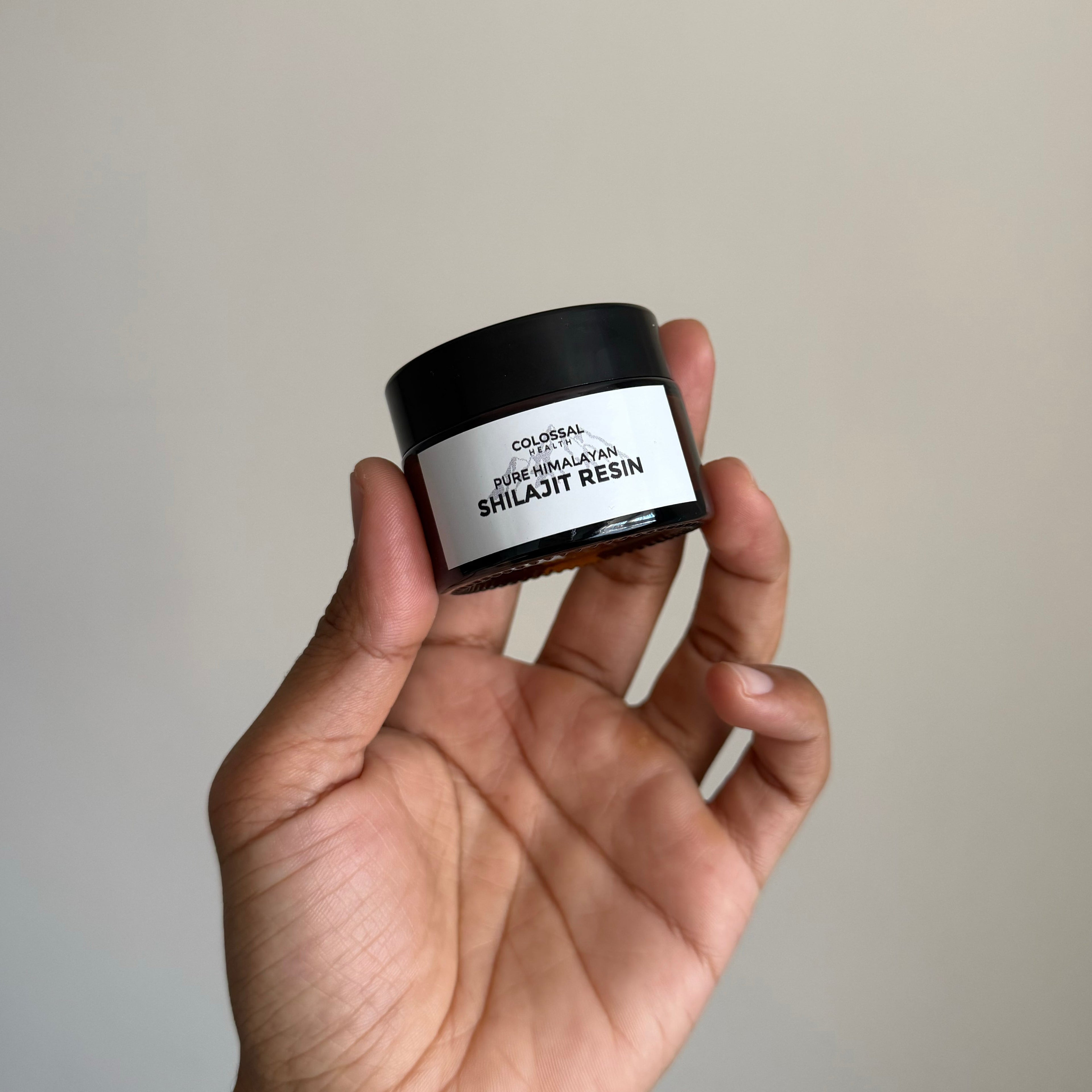 Hand holding a Colossal Health Pure Himalayan Shilajt resin jar against a plain background