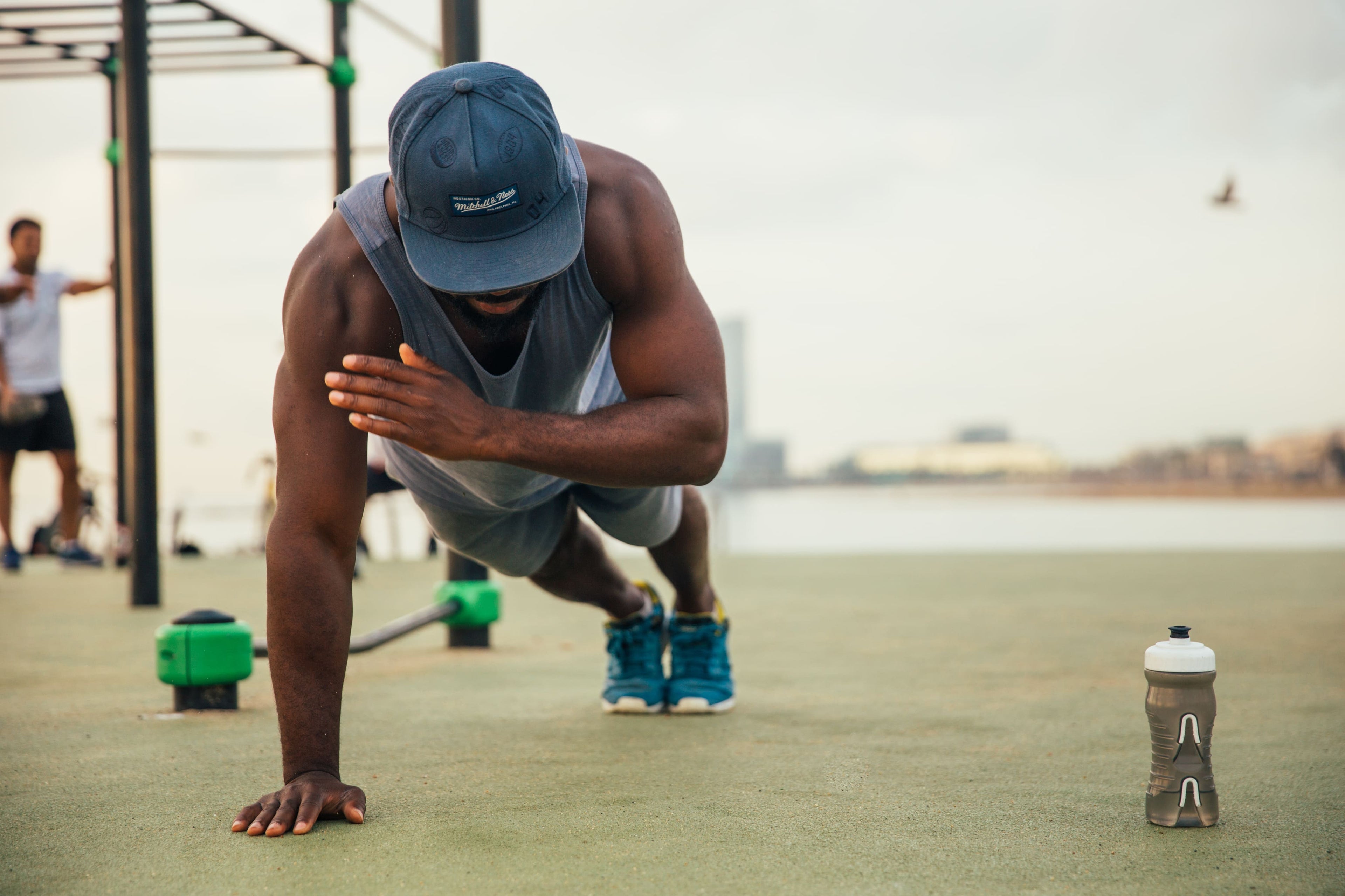 Man in athletic wear performing push-ups outdoors with a water bottle nearby.
